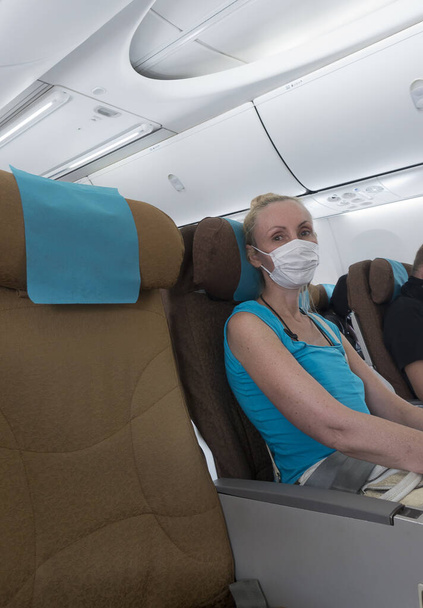 Woman in medical protective mask in the airplane. The adjacent chair is free to maintain distance. - 写真・画像