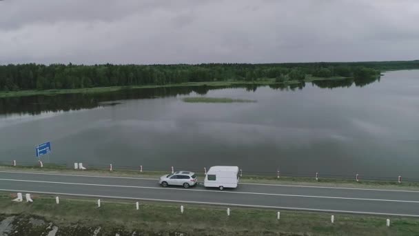 A car with a camper trailer rides along a dam across a river in Canada. Drone - Footage, Video