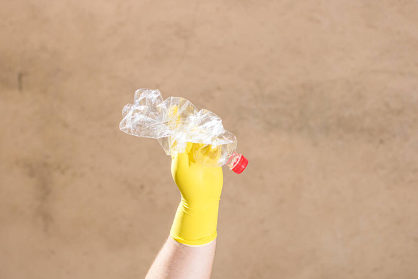 ゴム手袋を保持して手がぼやけた背景に隔離された壊れた空のプラスチックボトルを押します。リサイクルとボランティアのコンセプト。環境汚染と世界的な生態系の問題 - 写真・画像