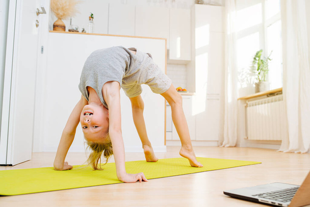 Cute little boy doing full bridge exercise, looking at camera. Physical athletic exercise on isolation at home. - Foto, Bild