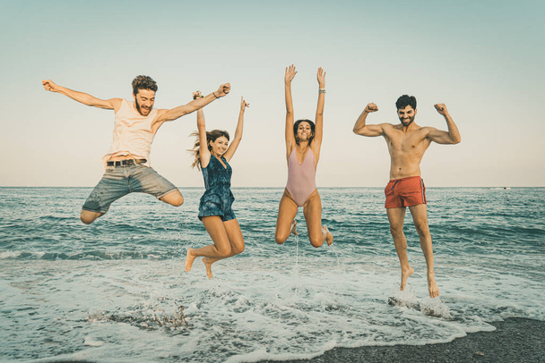 group of young adult people jumping on the seaside on vacation in the summer. vintage filtered image of couples of best friends having fun during the holidays.  - Photo, image