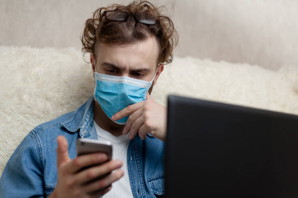 The guy is watching the news on his smartphone. Quarantine home environment. Epidemic of coronavirus. Social distance. Bad news. False news. - Photo, Image