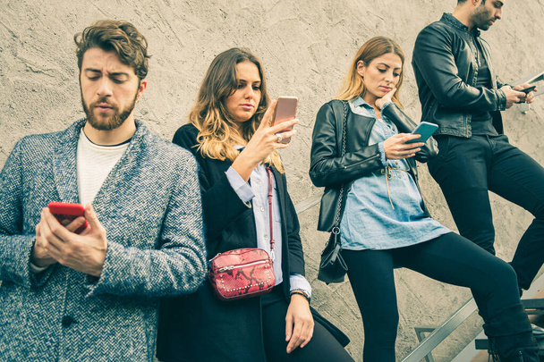 Trendy, Modefreunde, die auf der Straße entsorgte Smartphones auf einer Treppe benutzen. Technologie-Konzept der Millennial Generation Menschen, die soziale Medien und das Internet überall nutzen. Stadtschuss. Vintage-Filter - Foto, Bild