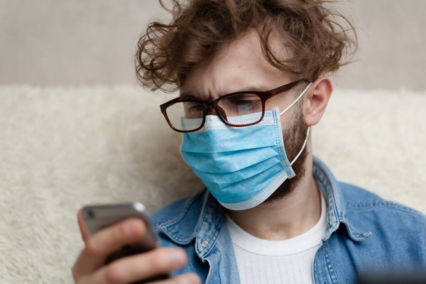 The guy is watching the news on his smartphone. Quarantine home environment. Epidemic of coronavirus. Social distance. Bad news. False news. - Фото, зображення