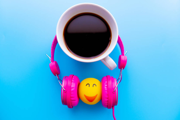 Top view the cup of coffee is listening music by pink headphones  on blue backgroudn with copy space. - Photo, Image