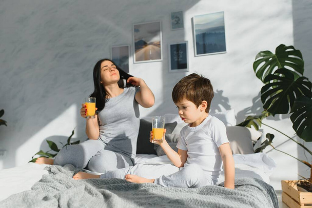 mom with son in pajamas drinking juice in the morning in bed. Healthy eating concept - Fotografie, Obrázek
