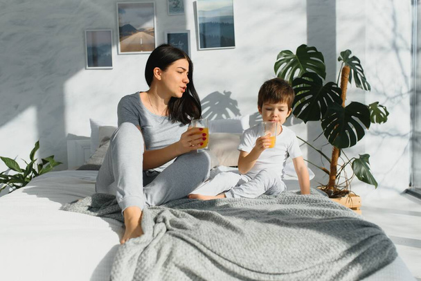 mom with son in pajamas drinking juice in the morning in bed. Healthy eating concept - Foto, imagen