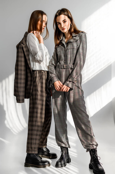 Two girls in a trouser suit and a check overalls on a white background - 写真・画像