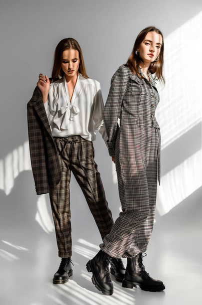 Two girls in a trouser suit and a check overalls on a white background - Фото, зображення
