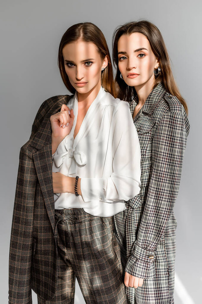 Two girls in a trouser suit and a check overalls on a white background - Фото, изображение