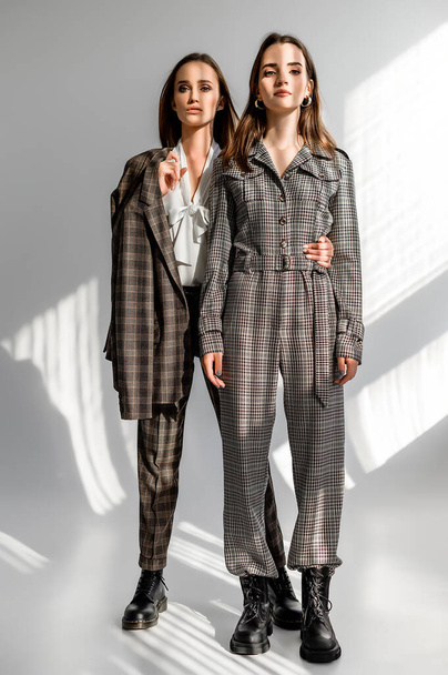 Two girls in a trouser suit and a check overalls on a white background - Фото, зображення