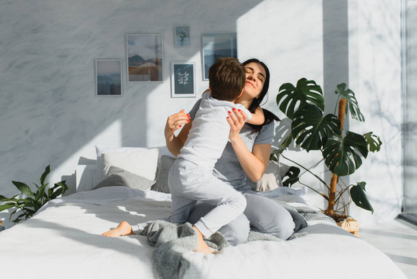портрет счастливой семьи, мама и ребенок в спальне, мать и сын обнимаются
 - Фото, изображение