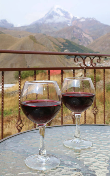 Deux verres de vin rouge sur une table en verre avec le mont Kazbek de Géorgie en arrière-plan
 - Photo, image