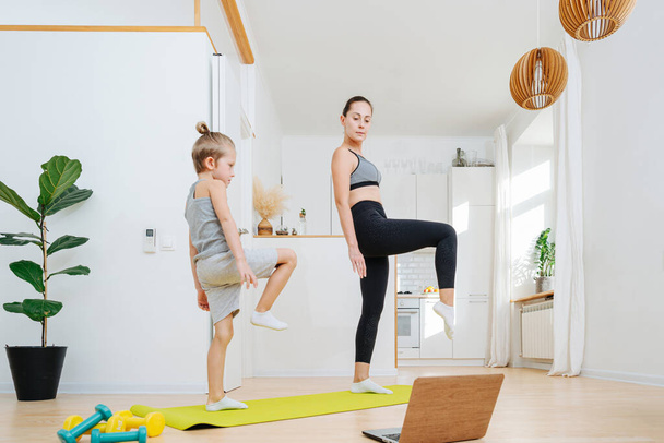 Mom and son doing yoga in front of a laptop at home, standing on one leg. Keeping fit while staying at home. Looking closely at screen. - Valokuva, kuva