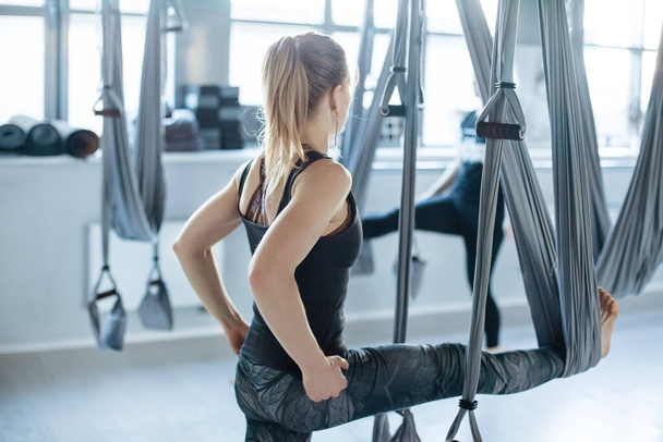 Een aantrekkelijke jonge vrouw doet stretching oefeningen met hangmatten in een Aero yoga Studio.Het concept van een gezonde levensstijl, plaats voor tekst - Foto, afbeelding