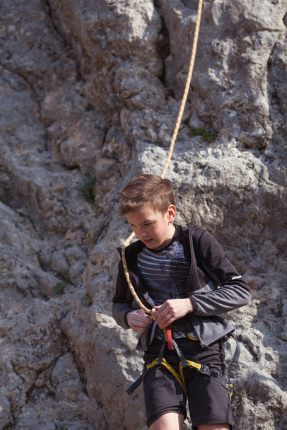 Nastolatek na skale zajmuje się wspinaczką skalną, sportem dziecięcym w przyrodzie, zajęciami plenerowymi dla dzieci - Zdjęcie, obraz