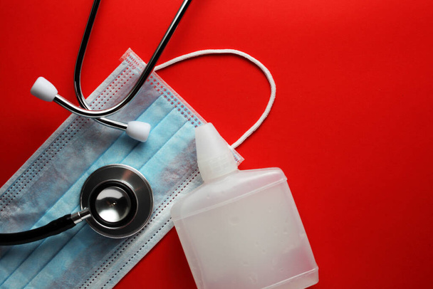 Medizinische Maske, medizinisches Phonendoskop, Antiseptikum auf rotem Hintergrund mit Platz für Ihren Text - Foto, Bild