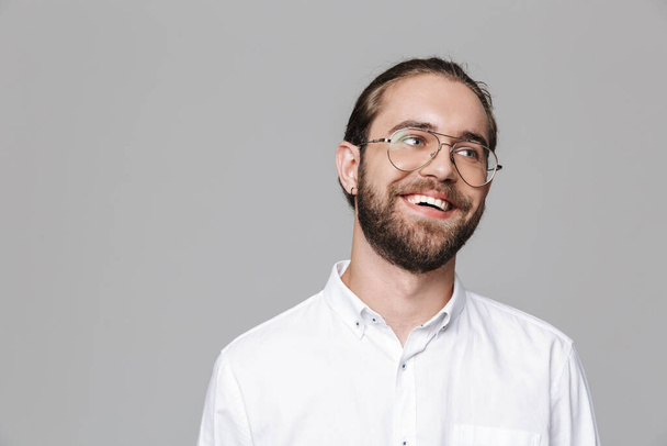 Image of a young cheerful happy handsome bearded man posing isolated over grey wall background wearing glasses. - Fotoğraf, Görsel