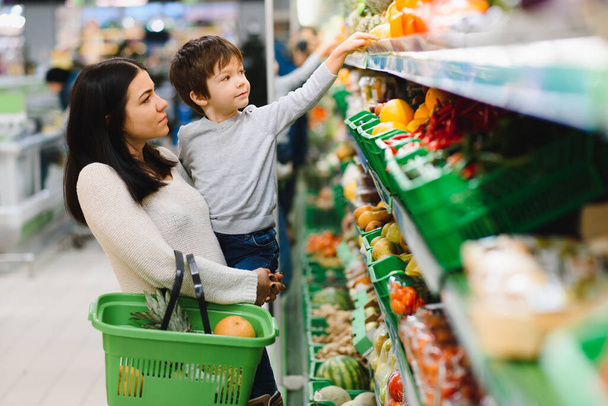 Young mother with her little baby boy at the supermarket. Healthy eating concept - Photo, image