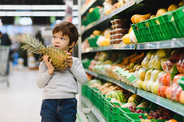 pretty boy with pineapple in supermarket - Photo, Image