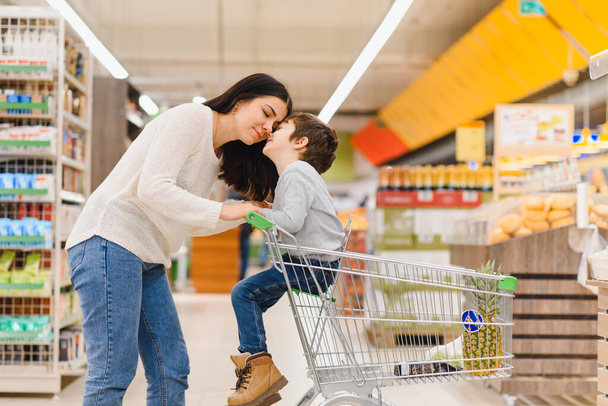 vrouw en kind jongen tijdens familie winkelen met trolley in de supermarkt - Foto, afbeelding