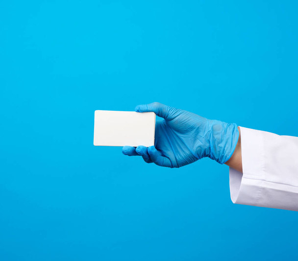 Kadın doktor elinde mavi tıbbi lateks eldivenler mavi arka planda boş bir kağıt kartvizit tutuyor. - Fotoğraf, Görsel