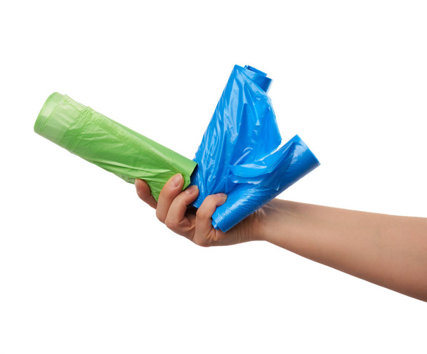 vrouwelijke hand houdt een bundel groene en blauwe plastic zakken voor vuilnis, een deel van het lichaam met het onderwerp geïsoleerd op een witte achtergrond - Foto, afbeelding