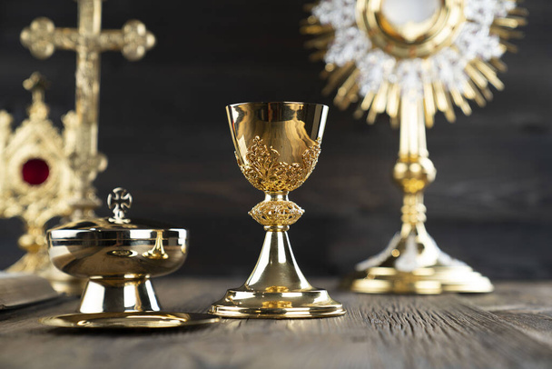 Catholic religion concept. Catholic symbols composition. The Cross, monstrance,  Holy Bible and golden chalice on wooden altar and gray background.  - Photo, Image
