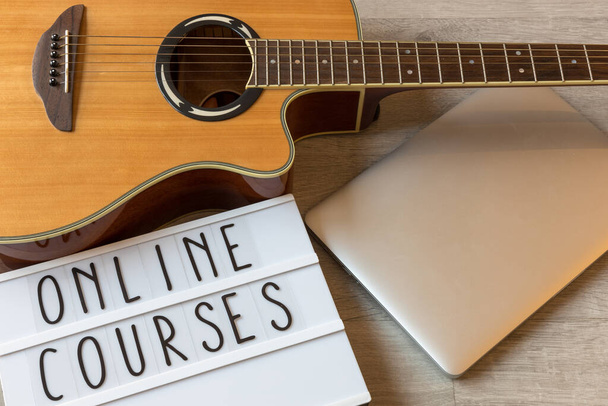 Гитара, ноутбук и доска с текстовыми "онлайн-курсами" для примера онлайн-уроков игры на гитаре
 - Фото, изображение