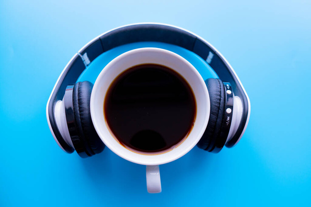 Headphones and coffee cup on blue background table. Music concept. Top view with copy space - Photo, Image