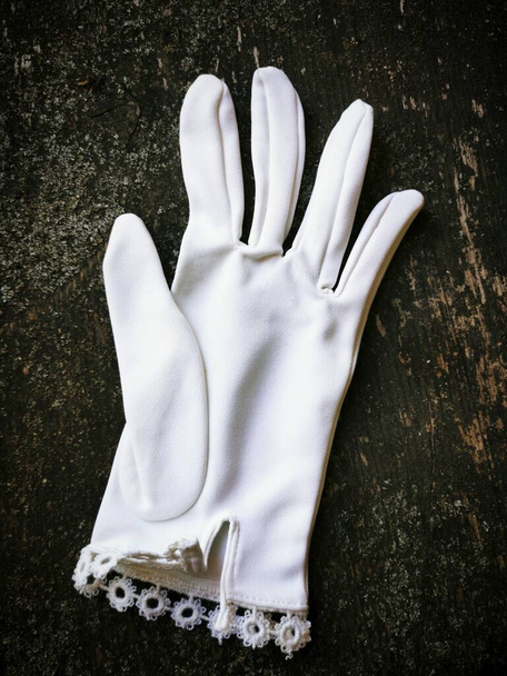 A vertical closeup of an elegant white glove on a wooden table under the lights - Photo, Image