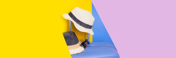 ブルー、ピンク、イエローのパステルの背景を持つ2つのヴィンテージ夏の帽子と現代の青い荷物からの夏の旅行のコンセプトでカラフルです - 写真・画像