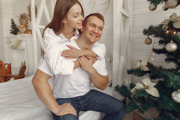 Elegant couple sitting on a bed near christmas tree - Foto, afbeelding