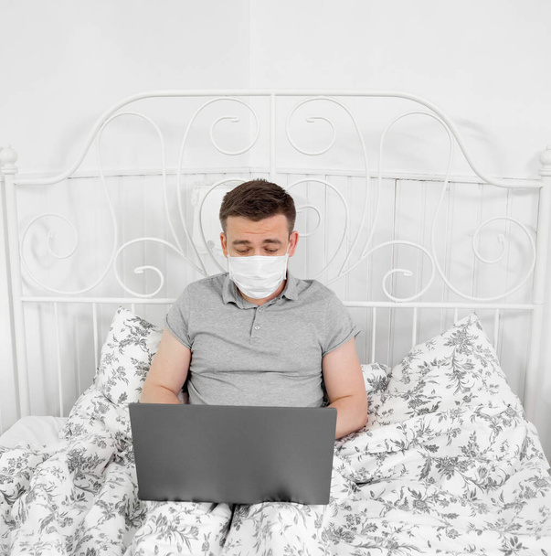 male freelancer in mask work from home in bedroom. - Foto, afbeelding