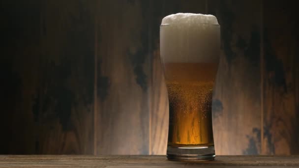 コピースペース付きの木の背景に冷たいライトビールを入れてください。ガラスの黄金のエール - 映像、動画