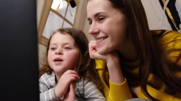 Happy young mom with kid daughter waving hands making distance video call looking at laptop sitting in tent at home, loving mother and cute child girl talking to webcamera chatting online - Кадри, відео