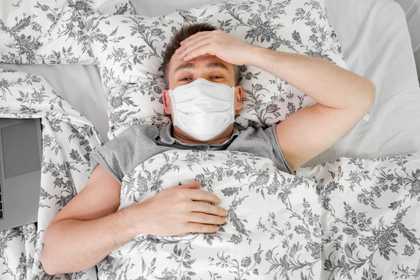 Человек в маске лежит дома в постели и болеет. остаться дома
 - Фото, изображение