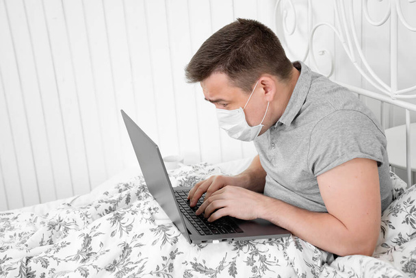 male in mask working from home in bed quarantine. - Foto, afbeelding