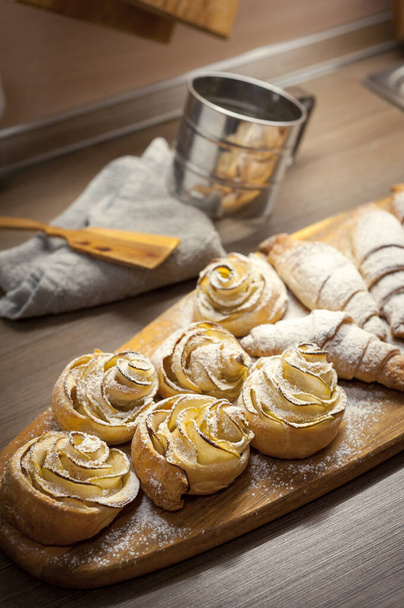 Großaufnahme von leckeren Croissants und Gebäck mit Äpfeln, auf einem Holzbrett in einem Café - Foto, Bild