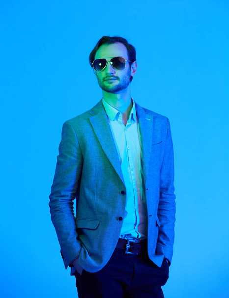 Elegant young handsome man in sunglasses and in stylish gray jacket. Studio fashion portrait - Foto, Bild