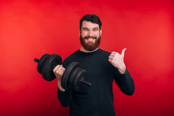 happy handsome young man holding dumbbell and showing thumbs up gesture - Φωτογραφία, εικόνα