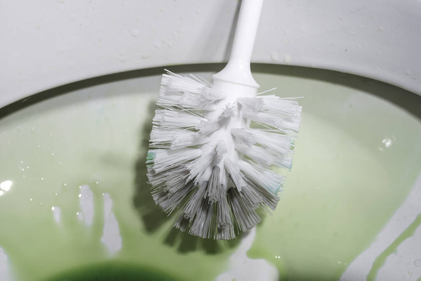 Pulizia della toilette con una spazzola da toilette utilizzando un disinfettante per la pulizia
 - Foto, immagini