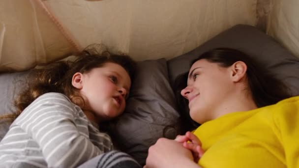 Affectionate family cute adorable funny little daughter embrace young mom lying relaxing in tent at home, happy mother and small girl enjoy bonding hugging. Self isolation, Home quarantine, pandemic - Materiał filmowy, wideo