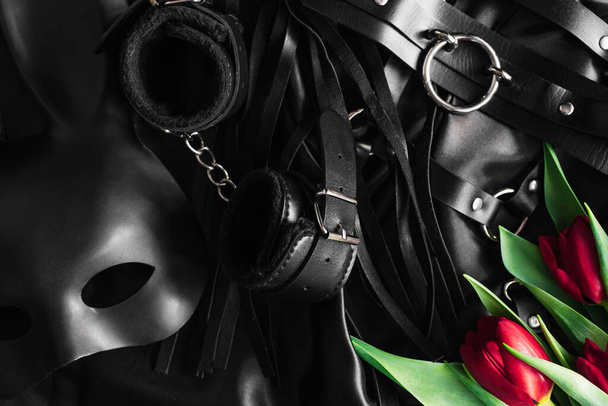 Explora el mundo del juego pervertido. Vista superior del kit de cuero bdsm contra de una seda negra. tulipanes
 - Foto, Imagen