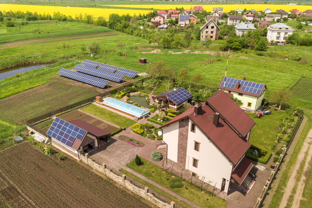Widok z lotu ptaka na prywatny dom w lecie z niebieskimi panelami słonecznymi fotowoltaicznymi na dachu i na podwórku. - Zdjęcie, obraz