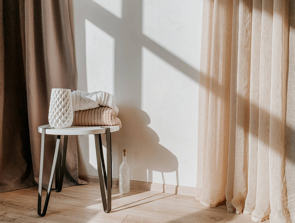 Άνετο Νεκρή Ζωή στο διαμέρισμα ηλιοφάνειας. Βάζο και πουλόβερ με κάποια διακόσμηση σε λευκό τραπέζι - Φωτογραφία, εικόνα