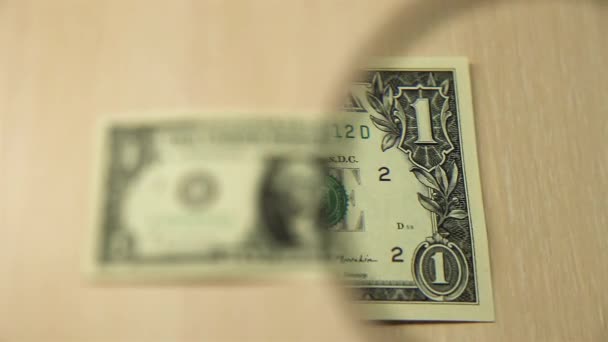 Δείτε ένα χαρτονόμισμα ενός δολαρίου ΗΠΑ που βρίσκεται σε ένα τραπέζι με ένα μεγεθυντικό φακό. έννοια των επιχειρήσεων και των οικονομικών. Εμπρόσθια. - Πλάνα, βίντεο