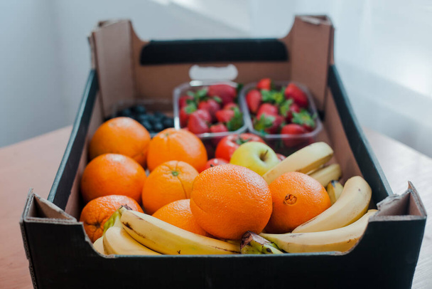 Παράδοση φρέσκων βιολογικών λαχανικών σε κουτιά, τοπικά τρόφιμα. Φρέσκα και πολύχρωμα λαχανικά και φρούτα σε ένα χαρτόνι. Πορτοκάλια, μπανάνες, μήλα, ντομάτες, φράουλες και μύρτιλλα. - Φωτογραφία, εικόνα