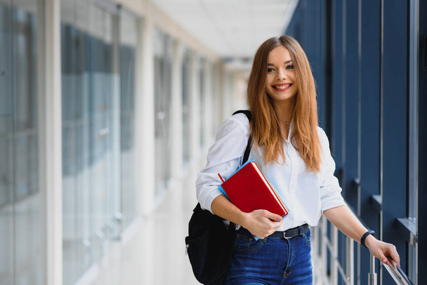 Positivity beautiful girl smiling at camera, standing on corridor with notes as backpack, going to lesson. Happy brunette female student studying in luxury university. - Zdjęcie, obraz