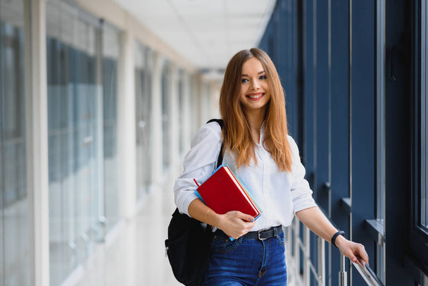 Portrait of a pretty female student with books and a backpack in the university hallway - Фото, изображение